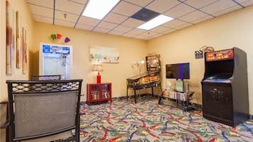 A room with a colorful arcade floor, a prize cube machine, a piano, and a television.