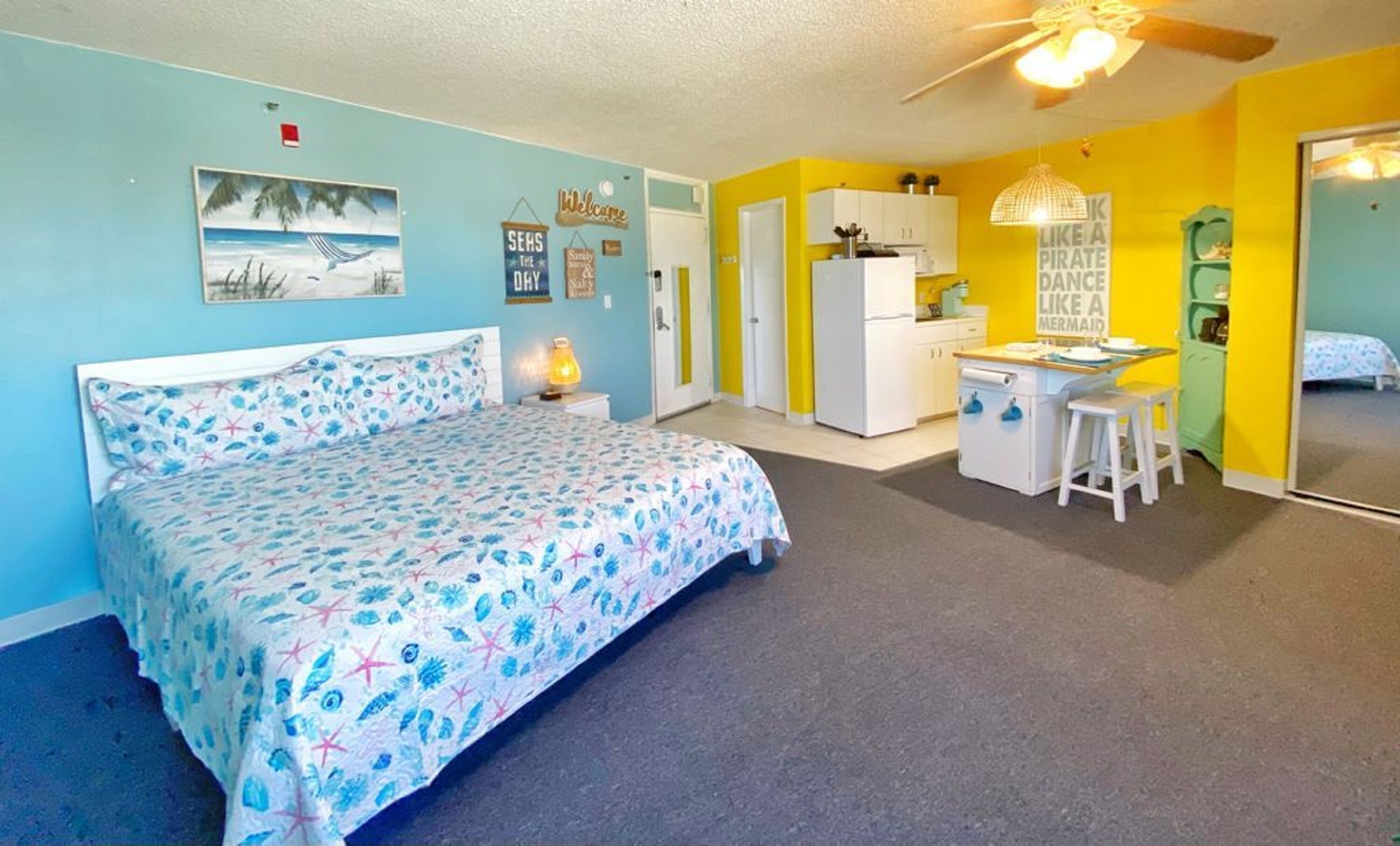 Quarto com cama, escrivaninha e cozinha compacta.