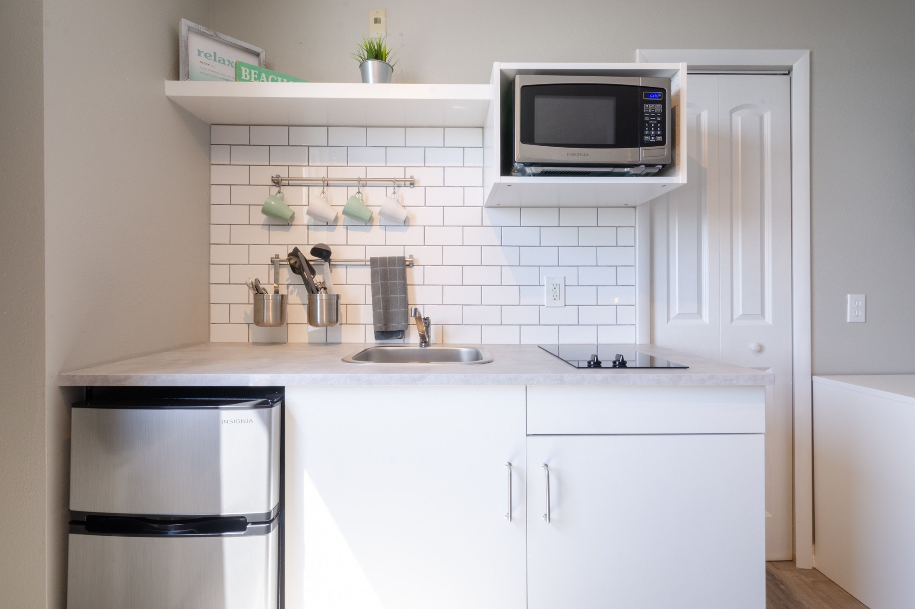 A modern kitchen with white cabinets, a stainless steel refrigerator, a microwave, and a sink.