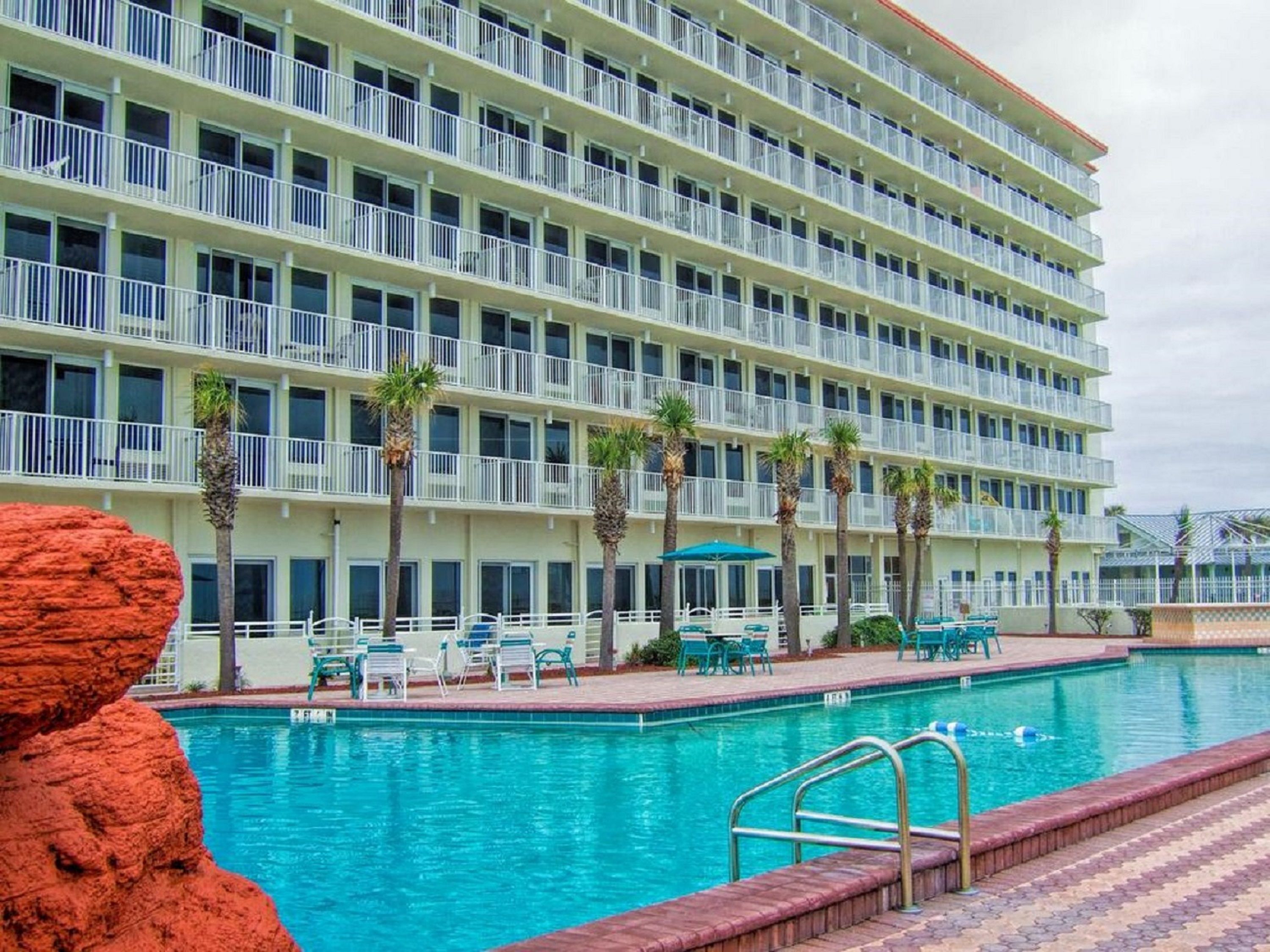Een meerlaags hotel met een zwembad, terras en palmbomen.