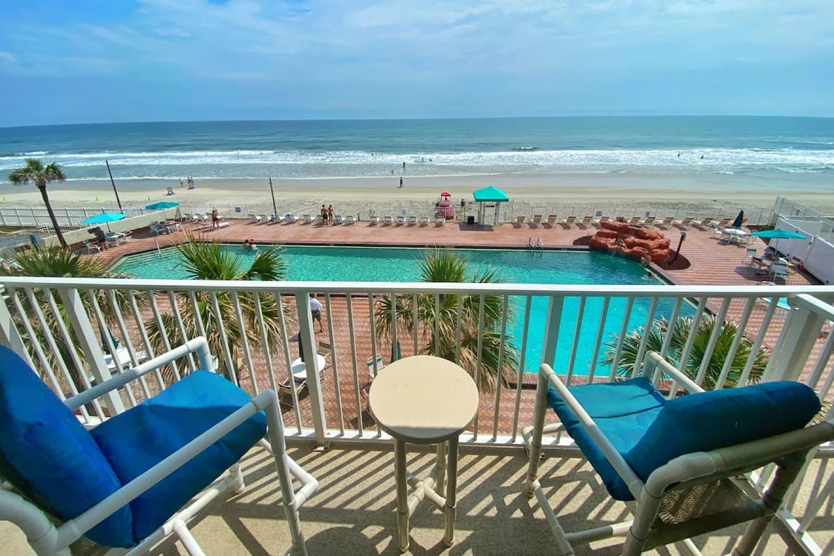A balcony with a pool and beach view.