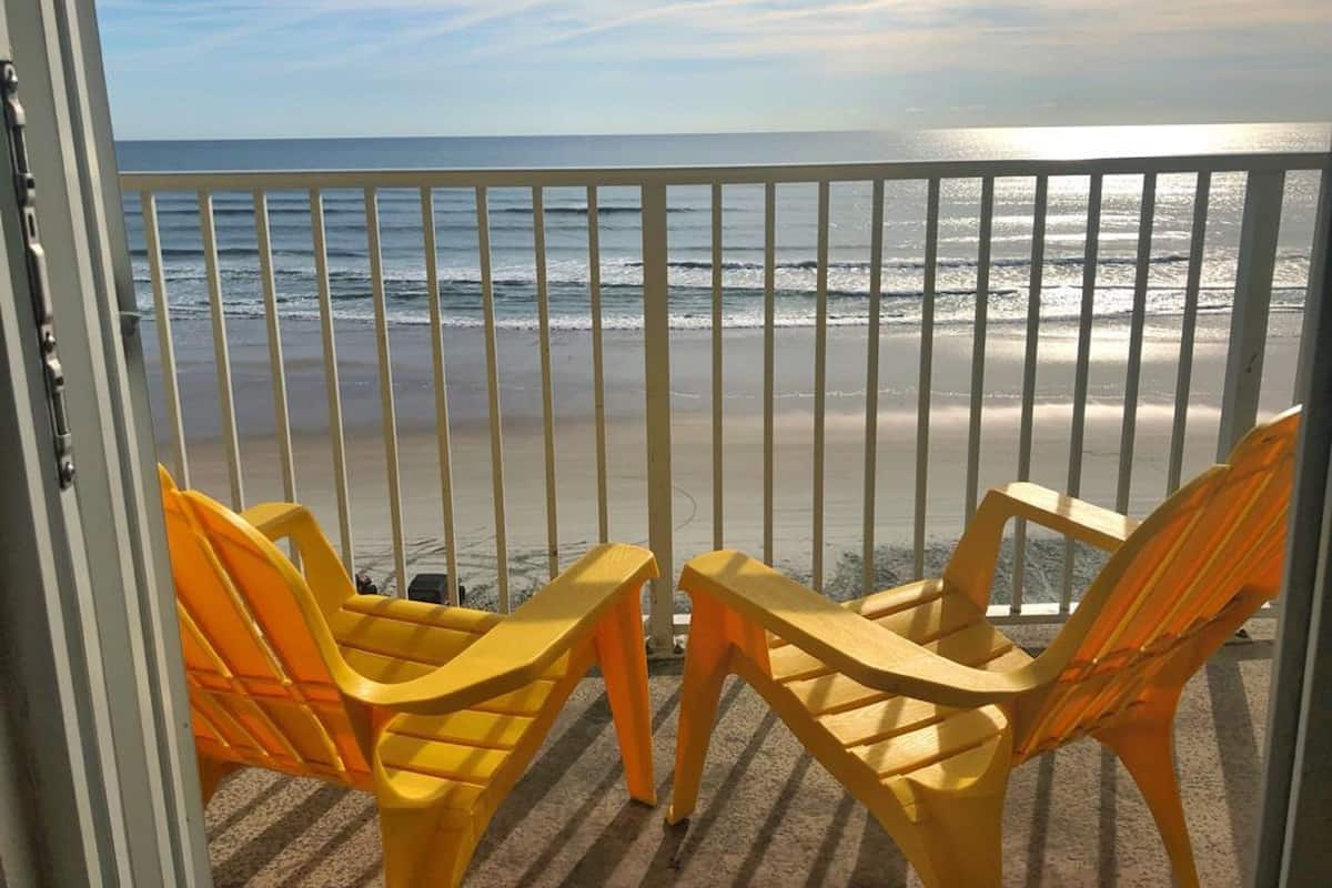 A balcony with two yellow chairs facing the ocean.