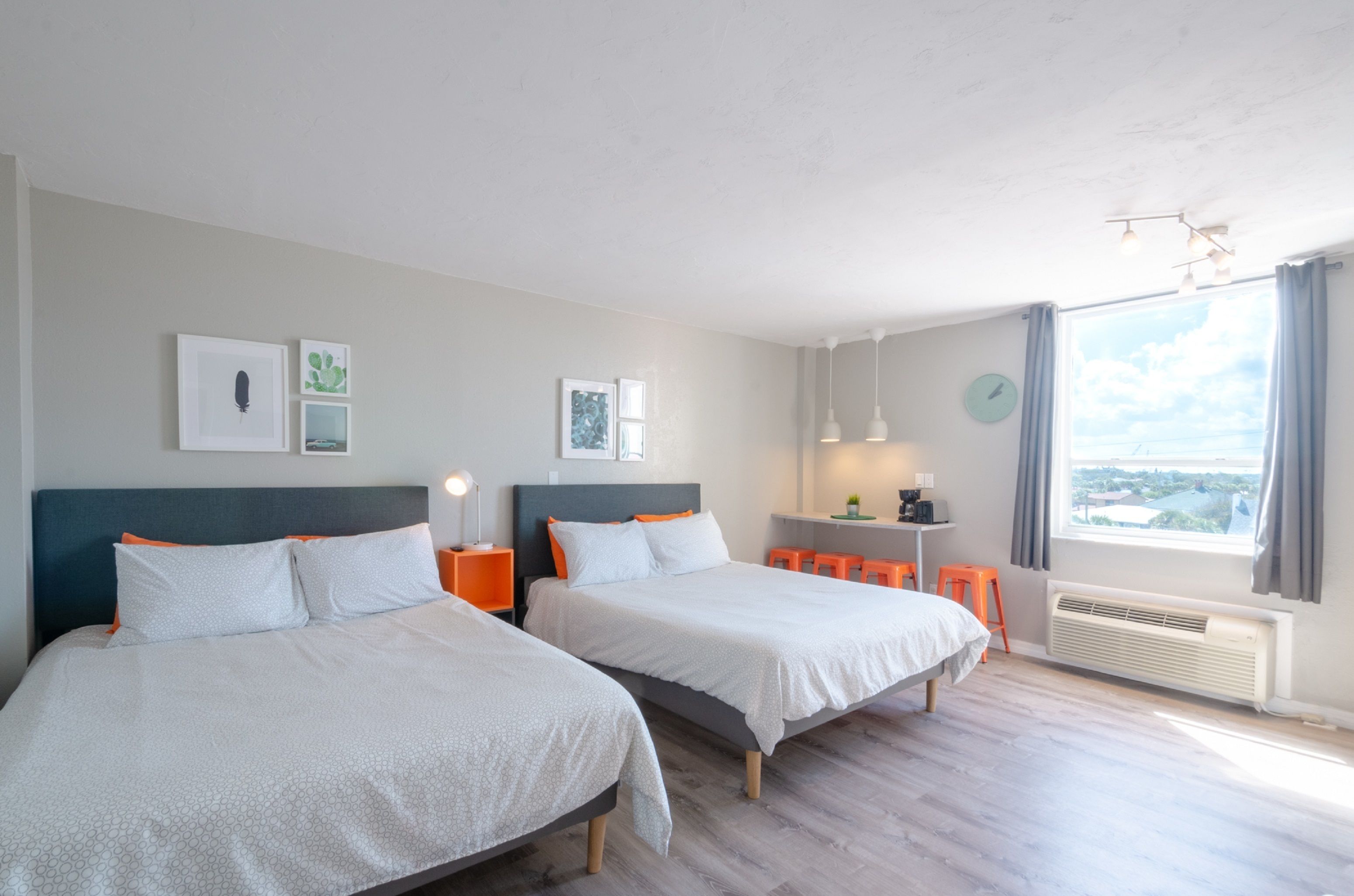 Une chambre d’hôtel moderne avec deux lits, un bureau, une chaise et une grande fenêtre donnant sur la ville.