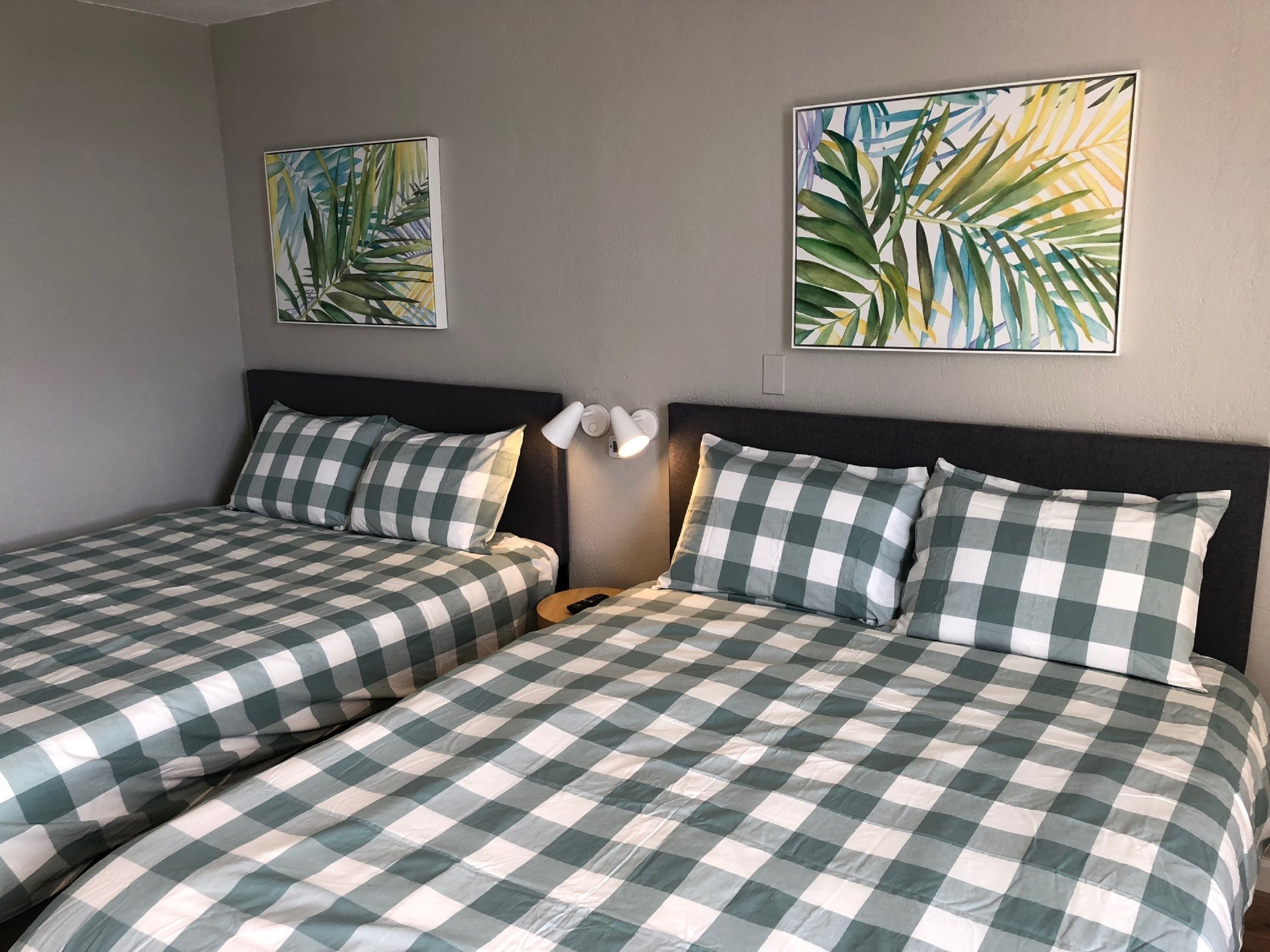 A hotel room with two beds, checkered bedding, a nightstand with a lamp, and two wall-mounted paintings.