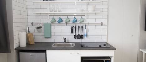A modern kitchen with white tiled backsplash, stainless steel appliances, and a shelf with kitchen utensils and plants.