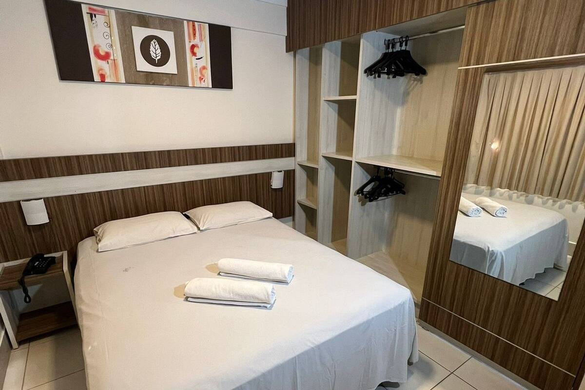 Habitación de hotel con cama, mesita de noche con teléfono, espejo y una pared decorada con obras de arte.