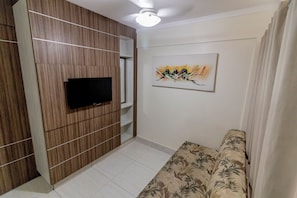 Uma sala de estar moderna com uma TV de tela plana fixada em uma parede revestida de madeira, um sofá estampado com motivos florais e uma obra de arte abstrata na parede.