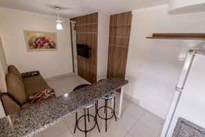 A kitchen with a granite countertop, two stools, a sofa, and a television.