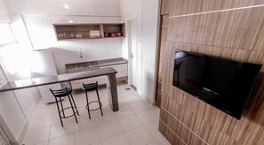 A modern kitchen with a TV, two bar stools, and a wooden shelf. - Lacqua Di Roma - JC Temporada (Caldas Novas)