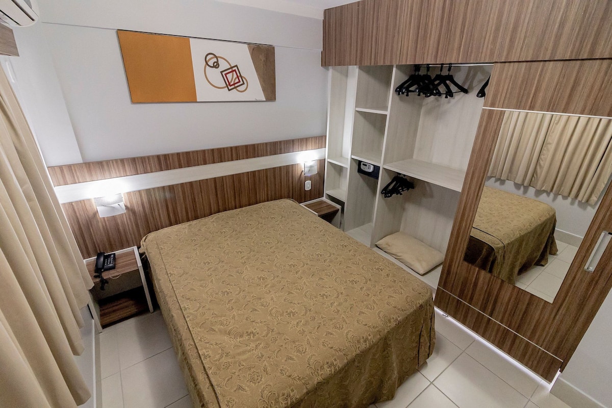 Un dormitorio con cama, armario con espejo, perchero y mesita de noche.