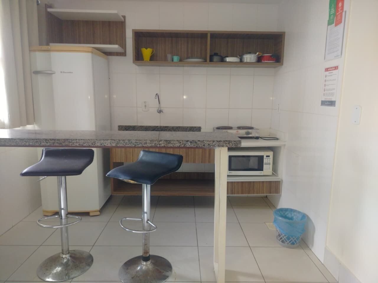 A kitchen with a white refrigerator, a microwave, and two blue bar stools.