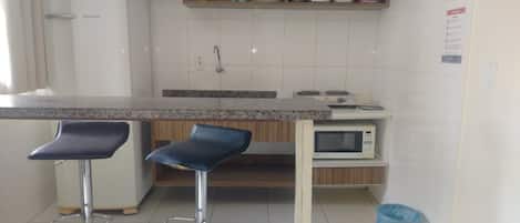 Una cocina con un refrigerador blanco, un microondas y dos taburetes azules.