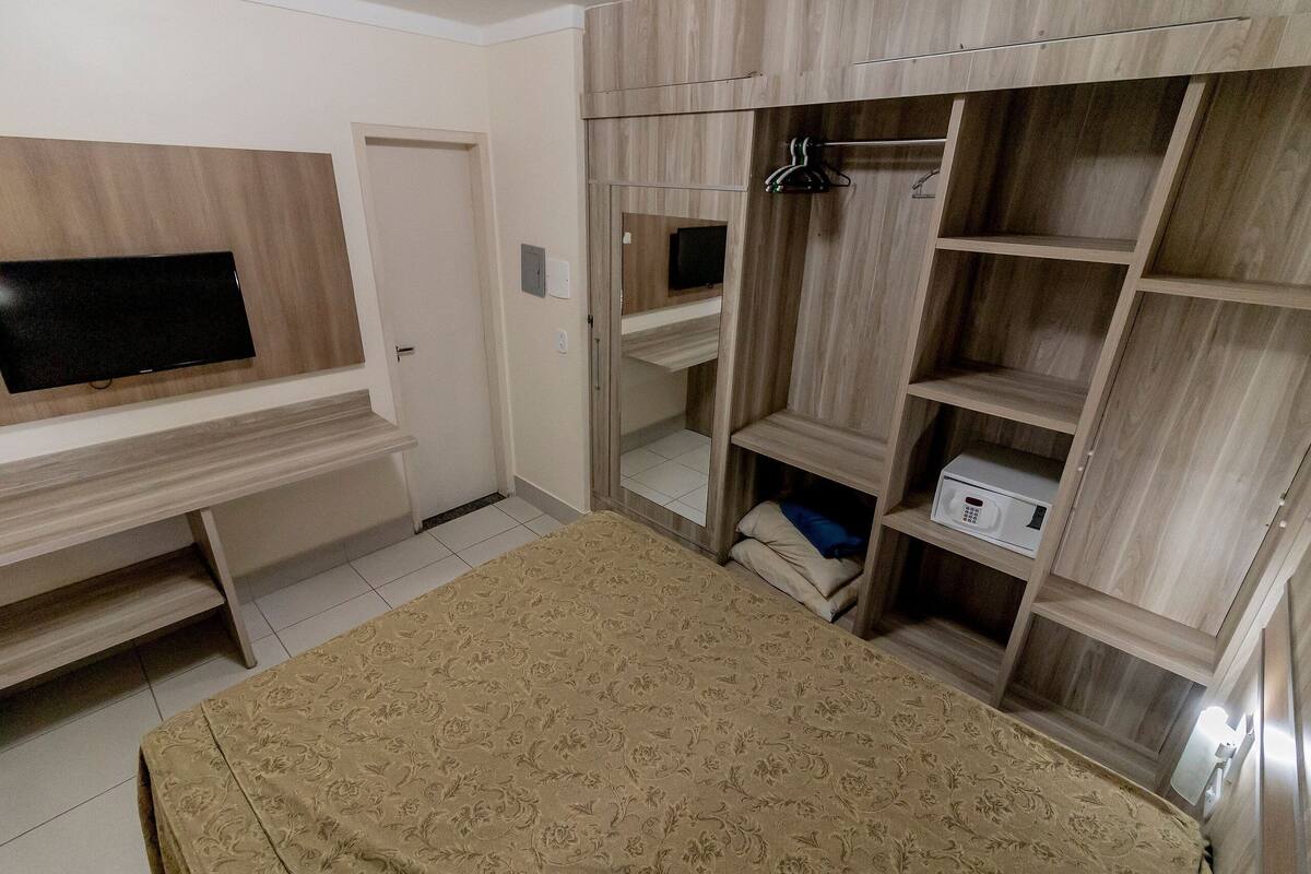 Un dormitorio con cama, televisor montado en la pared, armario con amplias estanterías y un escritorio pequeño.