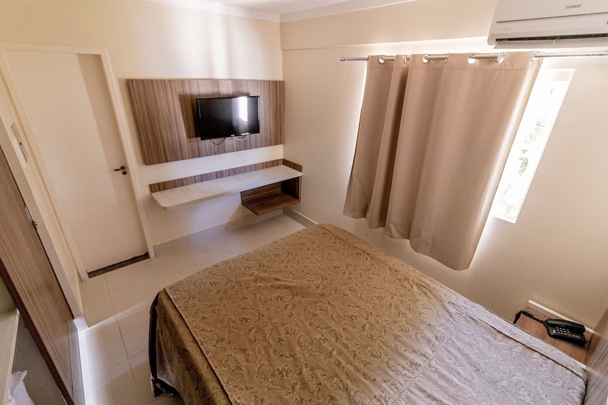 Un dormitorio con cama, televisor montado, cortina y termostato.