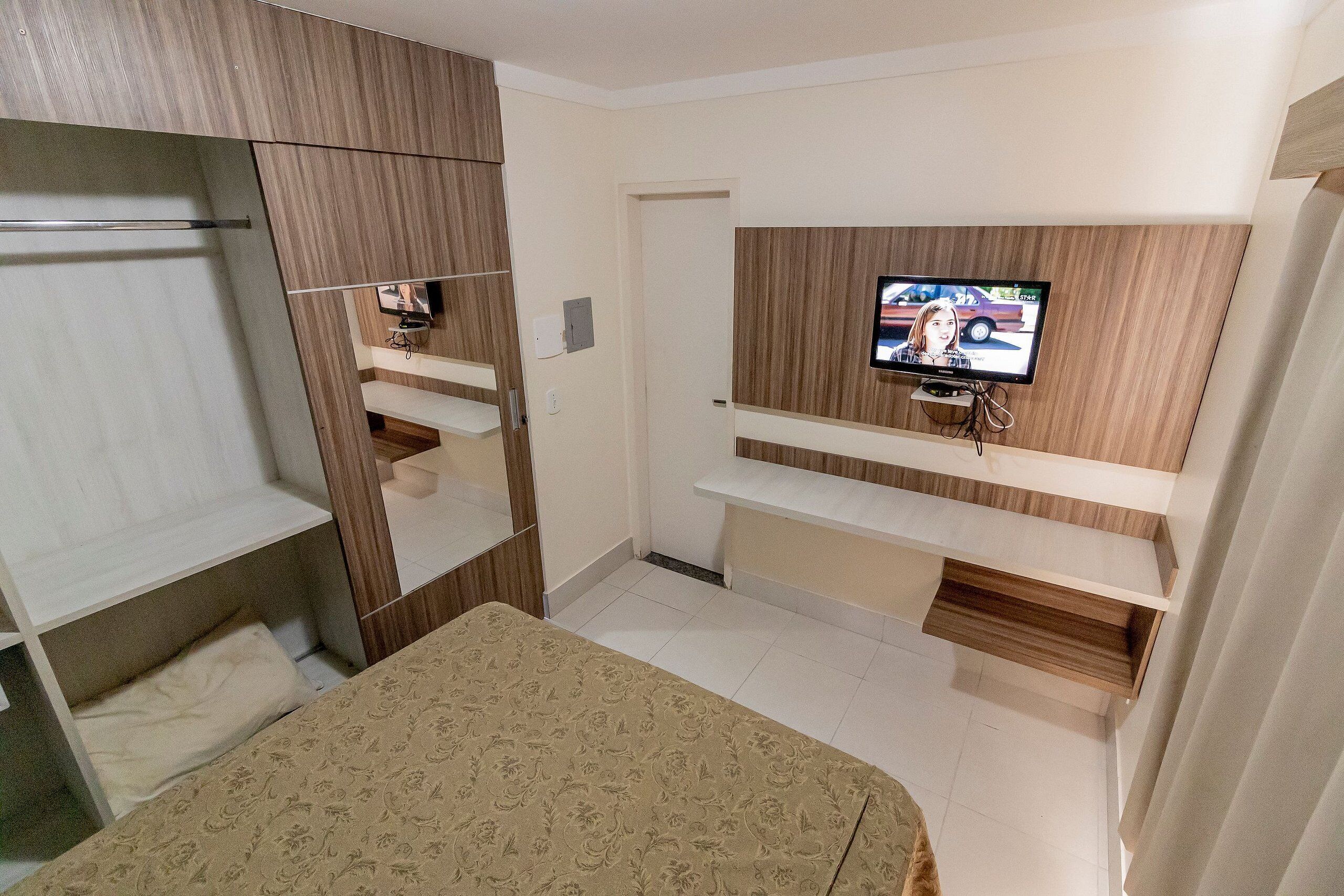 A bedroom with a bed, a TV mounted on the wall, and built-in shelving.