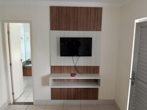 A room with a TV mounted on a wall, a wooden cabinet, and a white shelf.