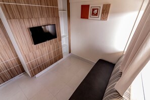 A room with a flat-screen TV mounted on a wooden panel wall, a sofa, and a small table. - Lacqua Di Roma - JC Temporada (Caldas Novas)