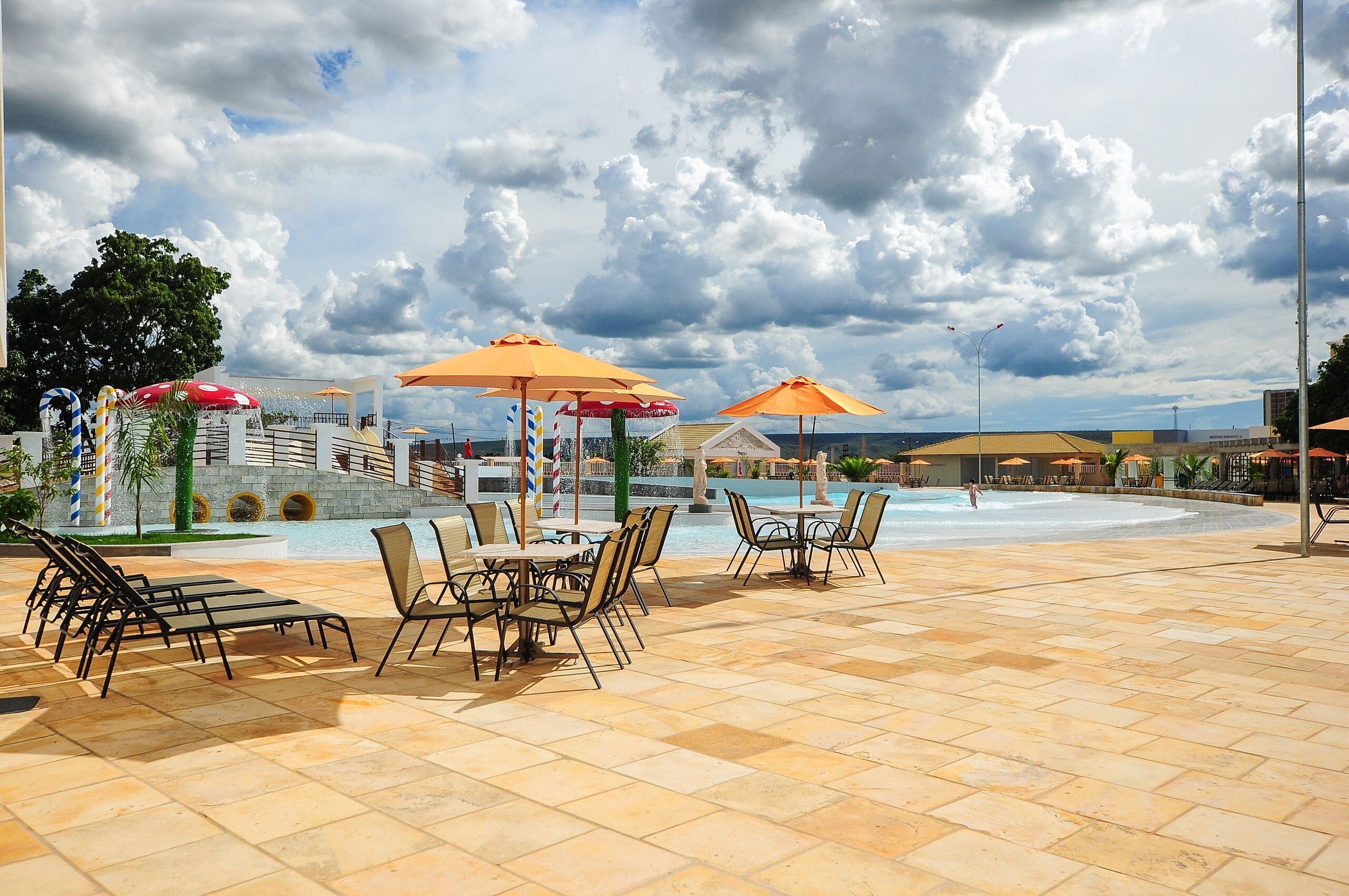 Zona de piscina con mobiliario exterior, sombrillas, una fuente de agua y vistas al cielo.