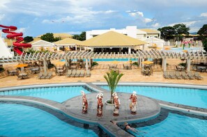 A pool area with multiple lounge chairs and umbrellas, a central statue, and a red slide. - Lacqua Di Roma - JC Temporada (Caldas Novas)