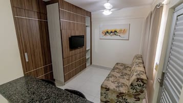 Un espacio habitable compacto con sofá, un televisor de pantalla plana montado en un mueble de madera, ventilador de techo y un cuadro en la pared.