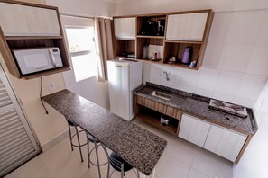 A compact kitchen with a microwave, refrigerator, and bar stools. - Lacqua Di Roma - JC Temporada (Caldas Novas)