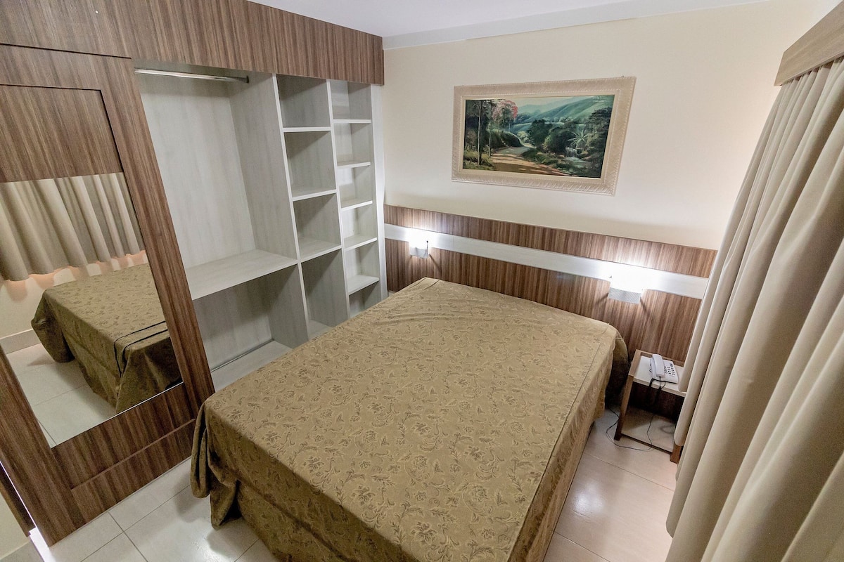 Un dormitorio con cama, armario, mesita de noche con teléfono y un cuadro en la pared.