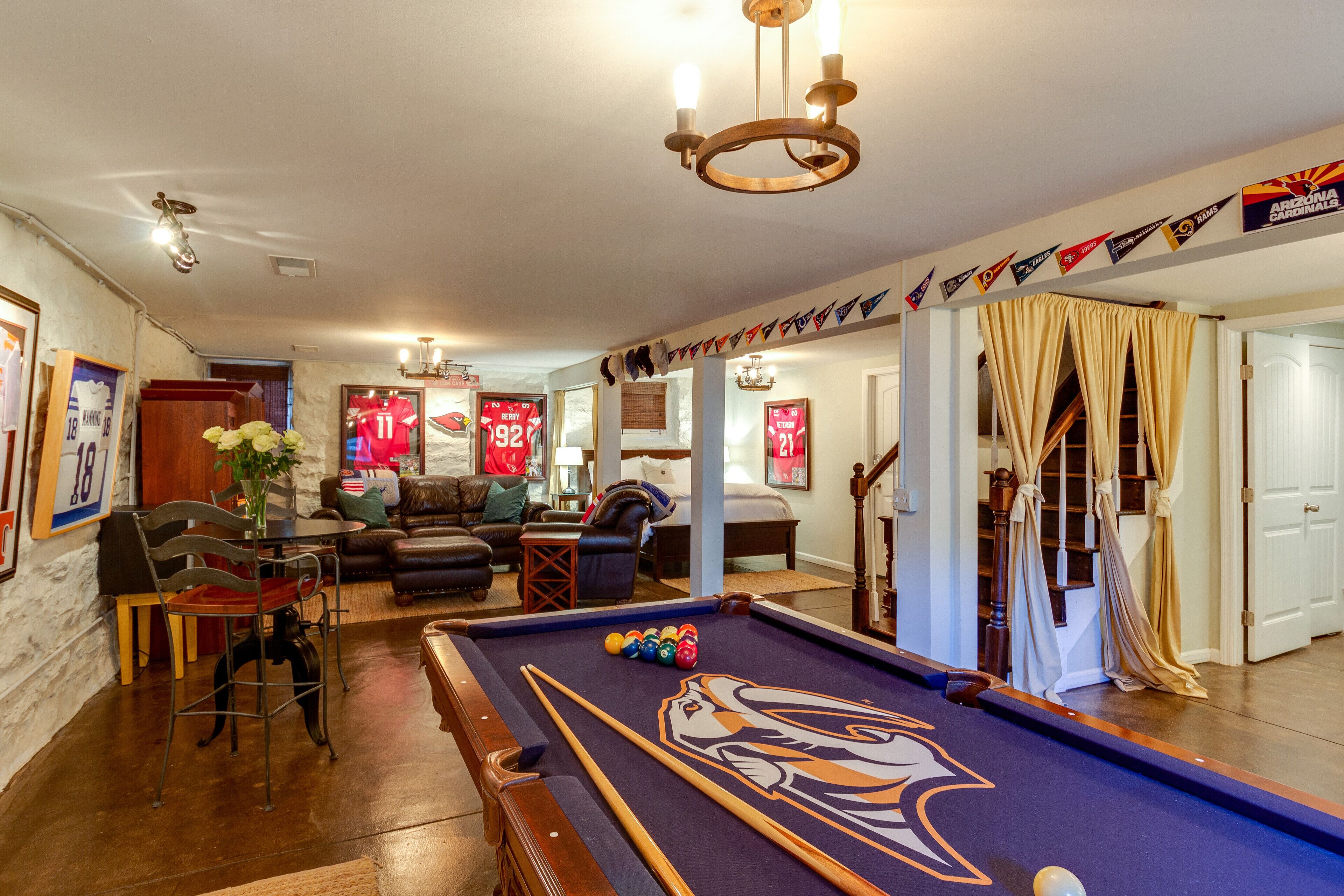 A pool table with a pool cue and balls, a sofa, a dining table with chairs, and a chandelier.