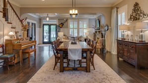 A spacious dining area with a long wooden table, surrounded by chairs, and a piano on the left.