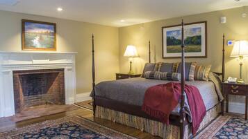 A four-poster bed with a red throw, a fireplace, two bedside lamps, and a large landscape painting above the bed.