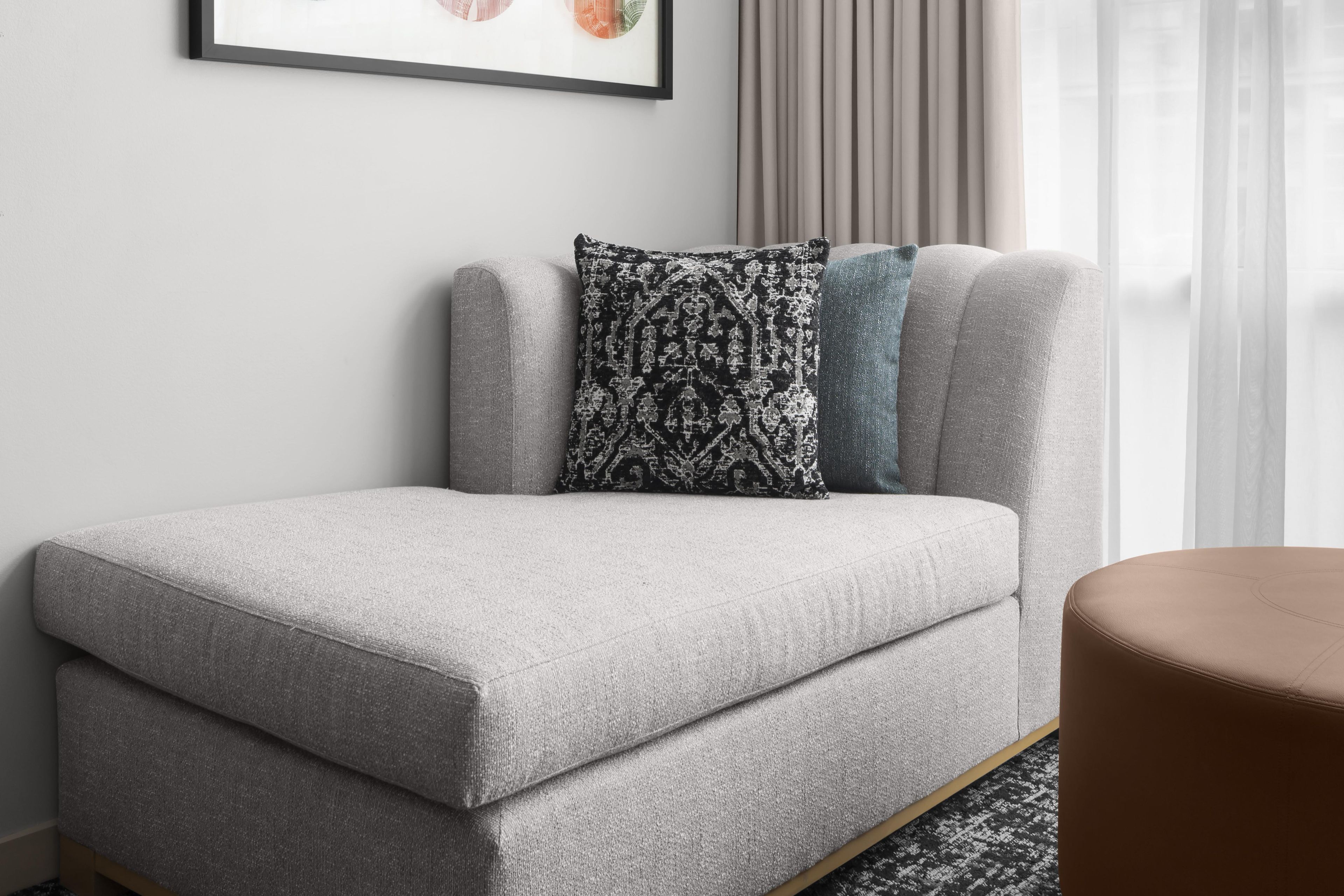 Ein graues Sofa mit einem gemusterten Kissen und einem blauen Akzentkissen, vor einer Wand mit einem gerahmten Bild platziert.