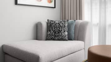 Ein graues Sofa mit einem gemusterten Kissen und einem blauen Akzentkissen, vor einer Wand mit einem gerahmten Bild platziert.