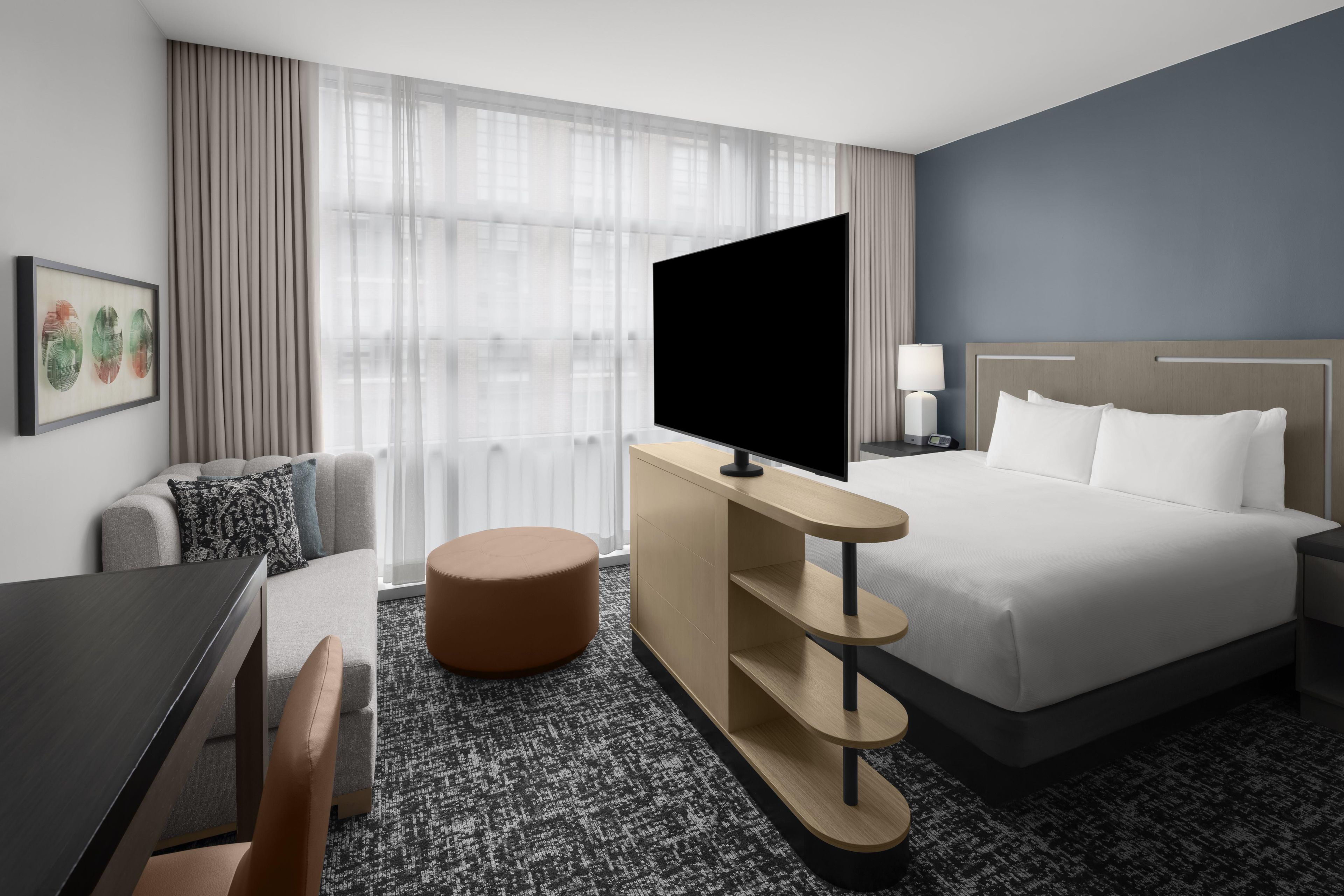 A hotel room with a bed, a desk, a TV, a sofa, and a window with curtains.