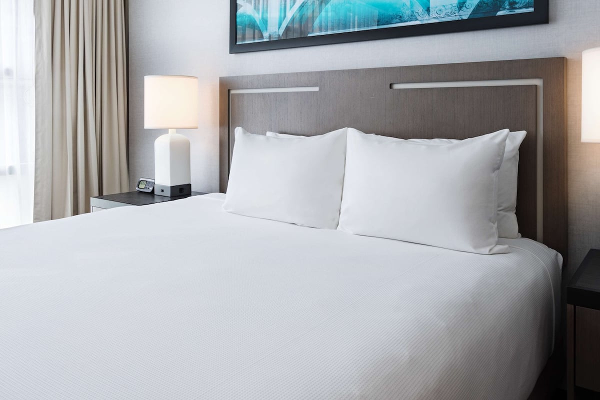 Una habitación de hotel con una cama grande, dos mesitas de noche y dos lámparas de pared.