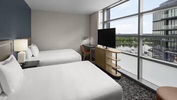 Habitación de hotel con dos camas, un escritorio, un televisor y vistas a un cuerpo de agua y edificios.