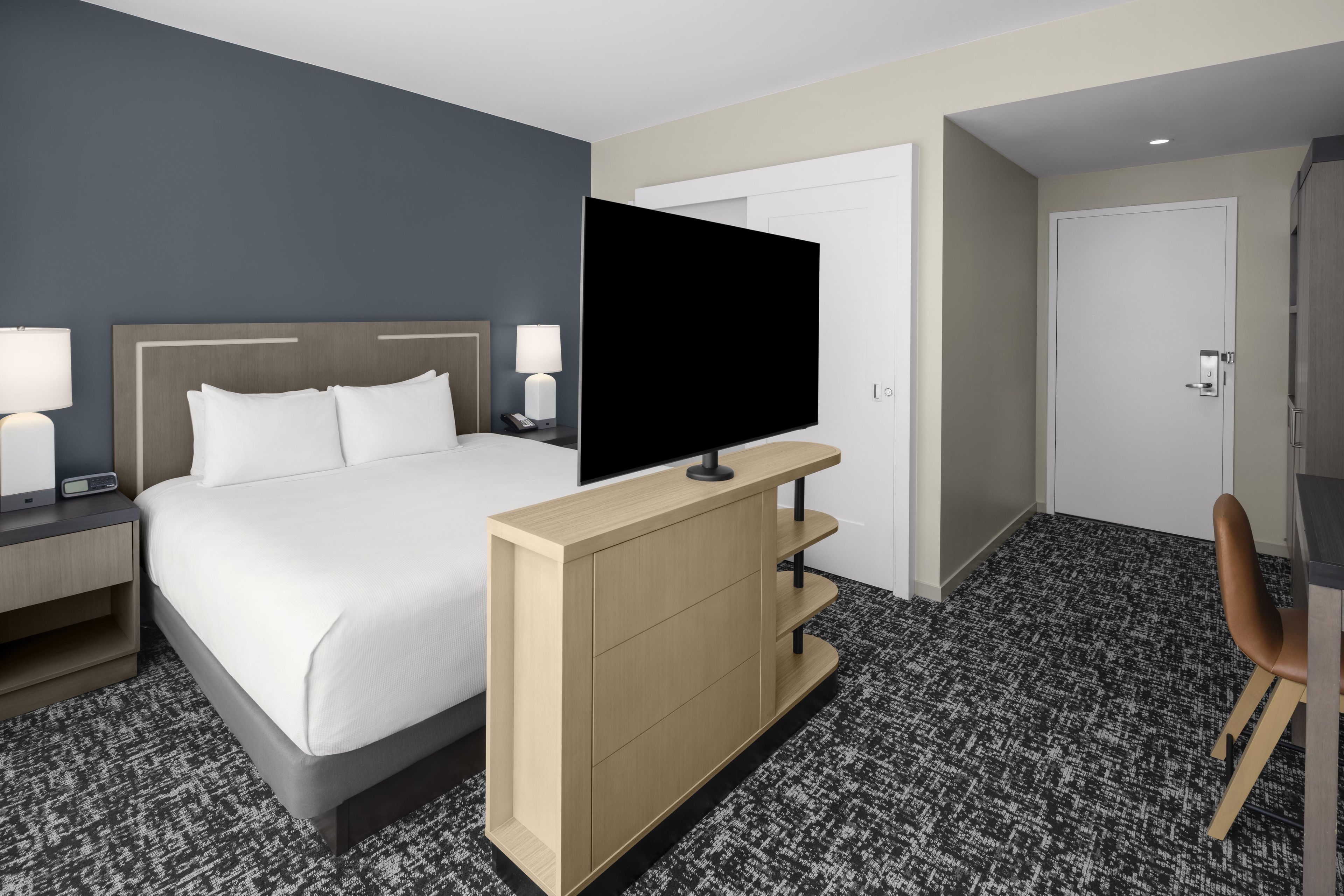Een hotelkamer met een bed, een televisie op een standaard, een bureau en een stoel.
