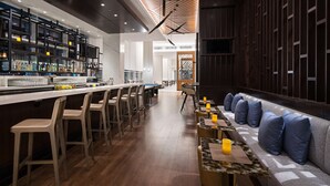 A modern bar area with a long counter, bar stools, and a seating area with cushions and tables.