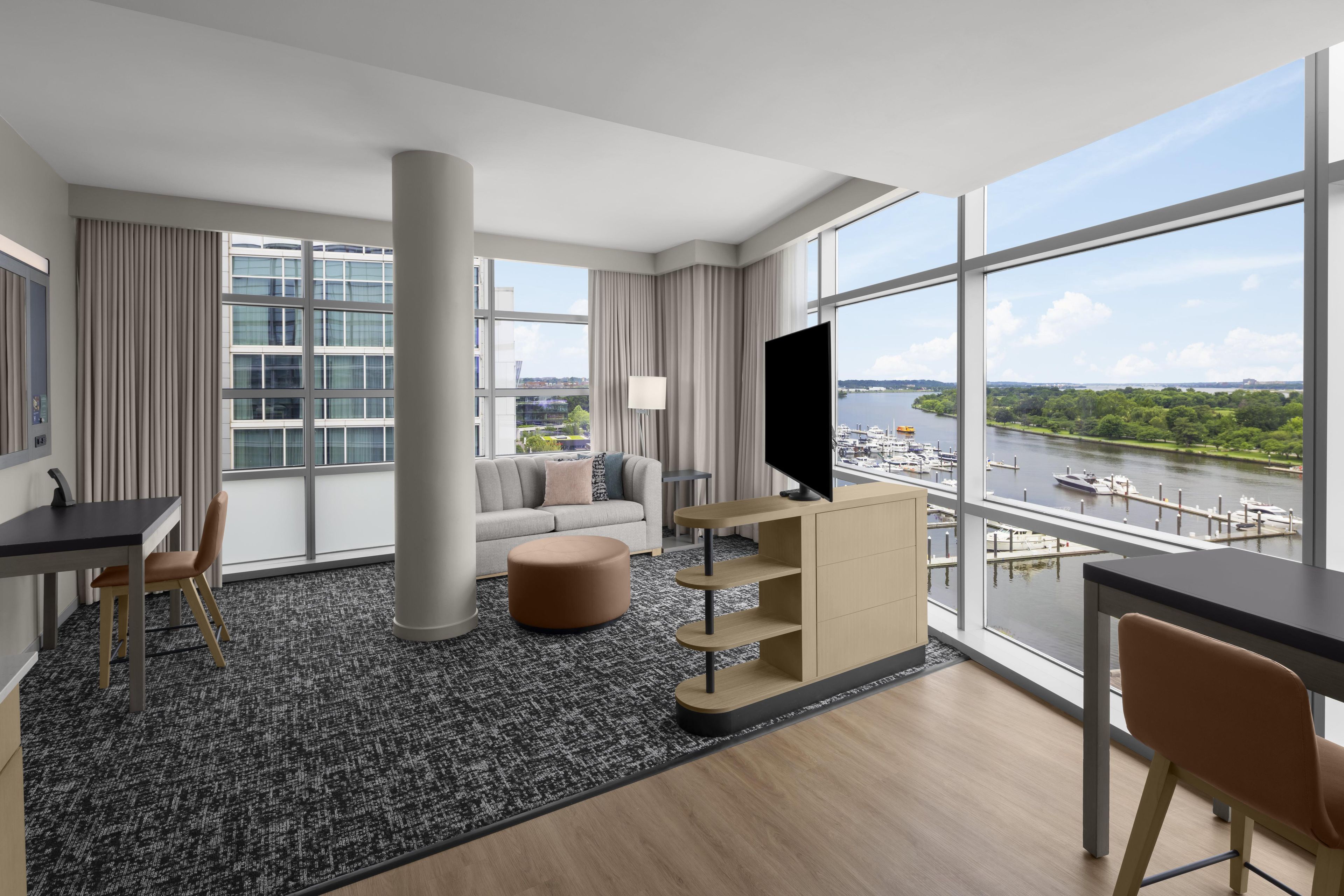 Een moderne hotelkamer met een groot raam, een bank, een televisie en een bureau.