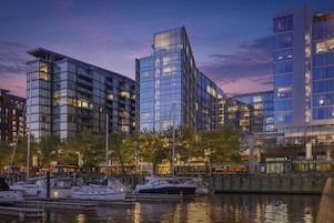 A waterfront marina with modern buildings, boats, and a clear sky.