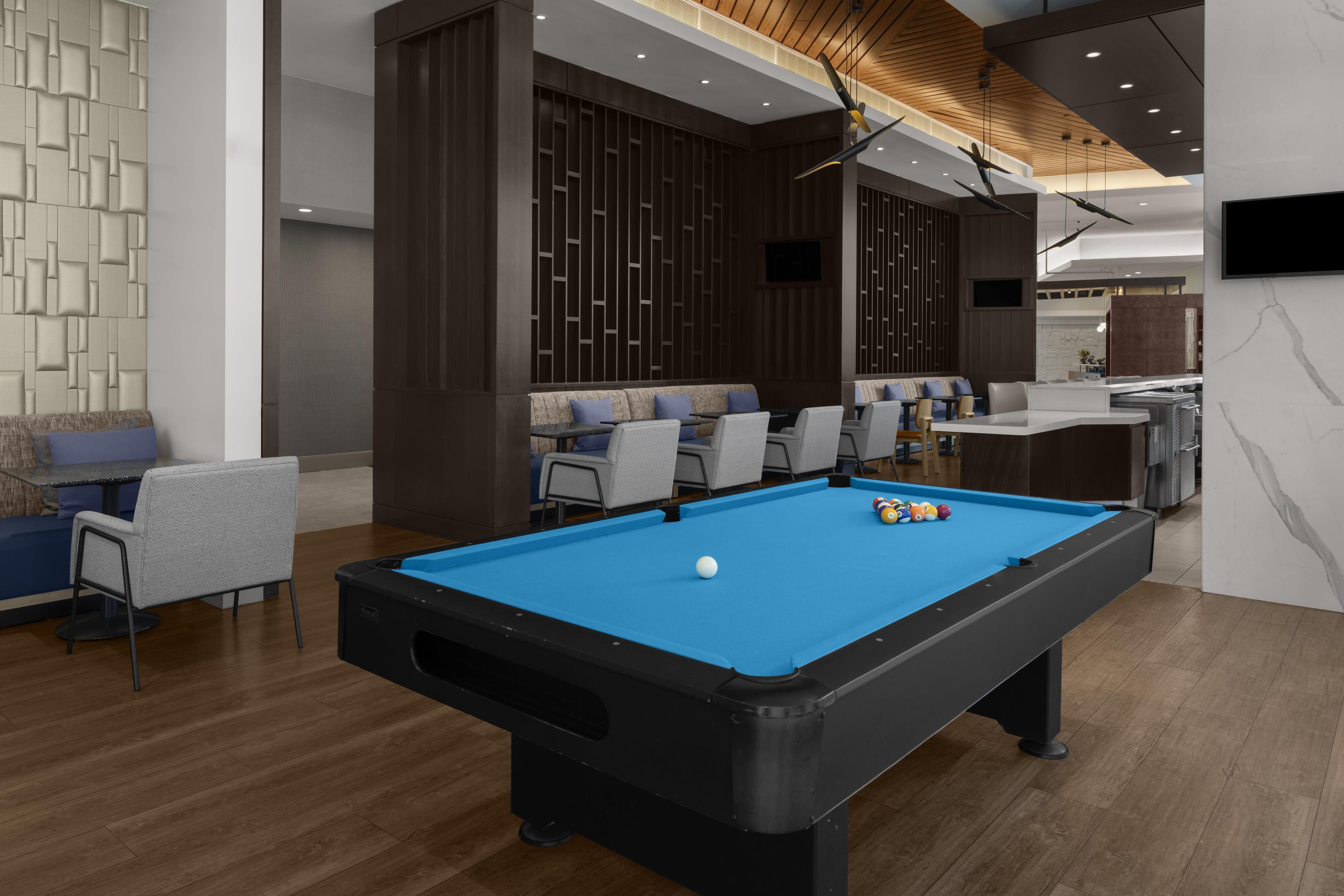 Une table de billard avec des billes, un coin salon avec des fauteuils et un téléviseur fixé au mur.