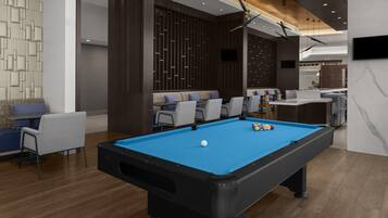 Une table de billard avec des billes, un coin salon avec des fauteuils et un téléviseur fixé au mur.