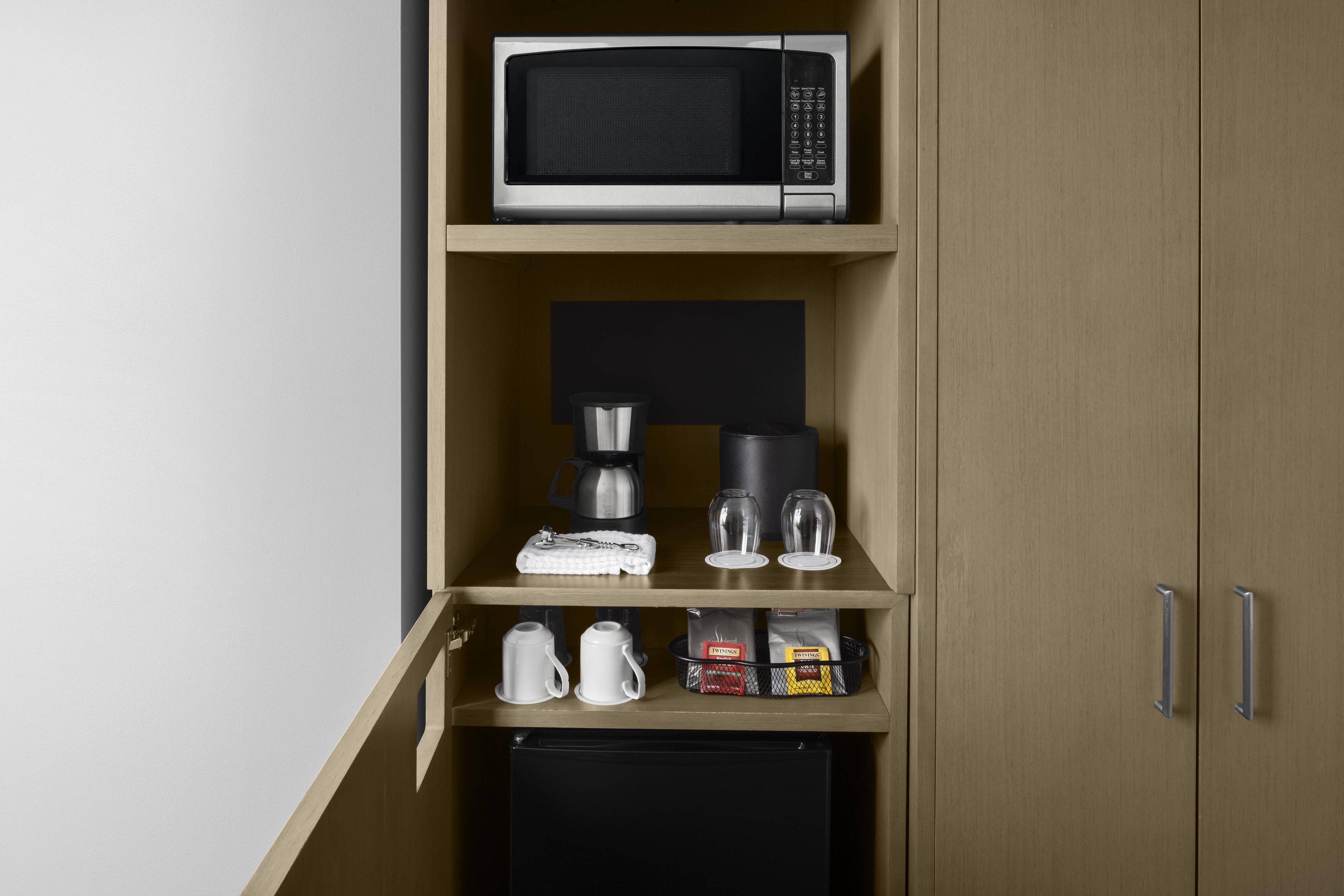 A kitchenette with a microwave, coffee maker, and tea bags.