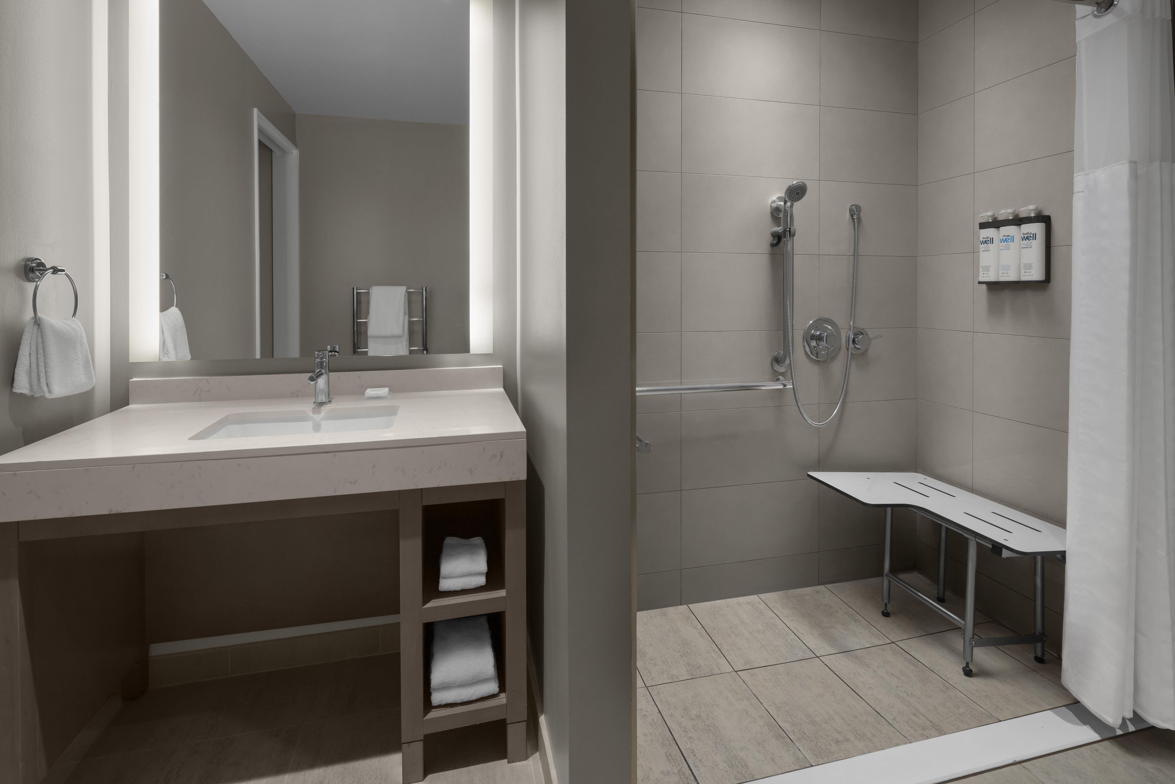 A modern bathroom with a sink, mirror, towel rack, shower, and a shelf with toiletries.