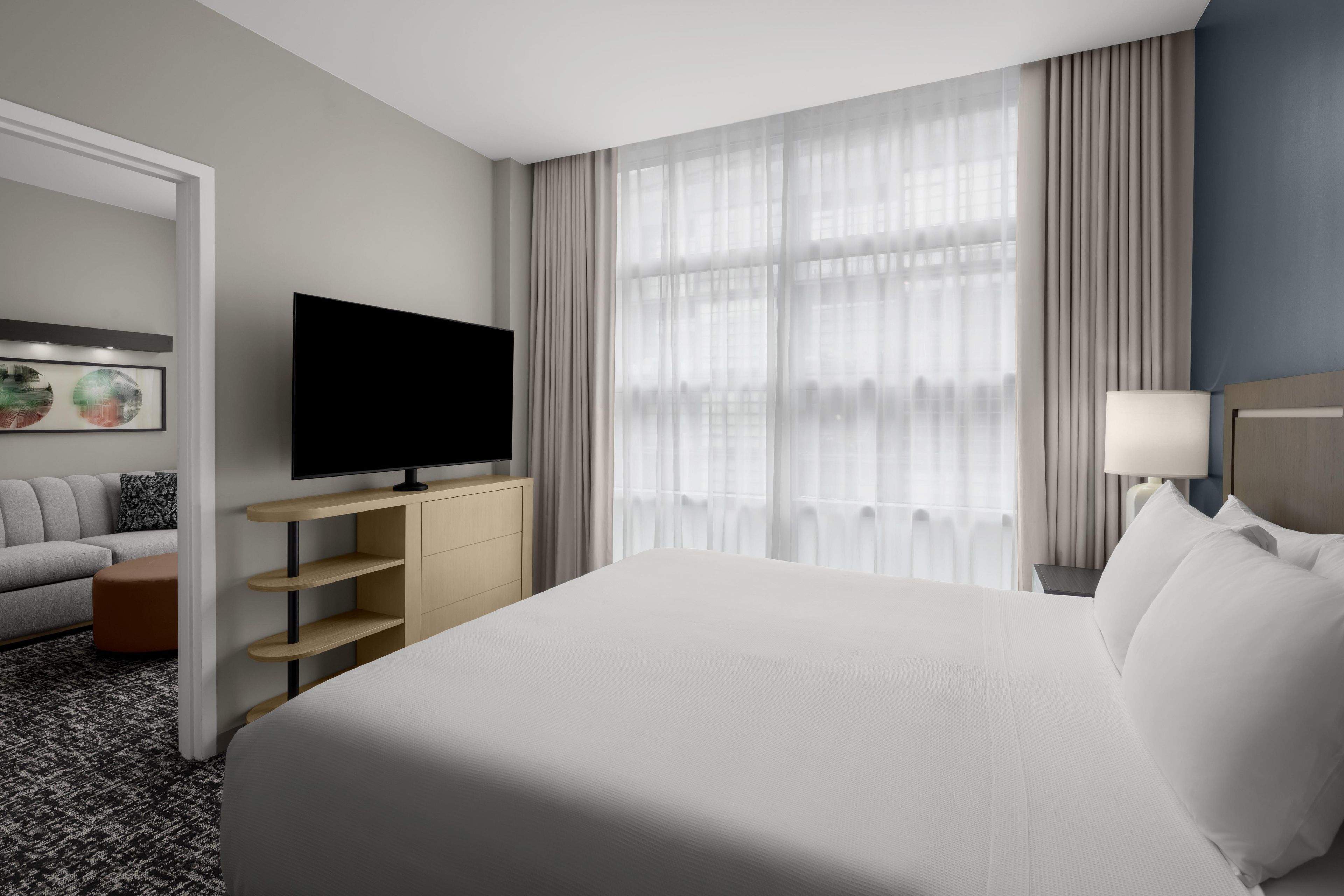 A hotel room with a bed, a TV, a sofa, a desk, and a window with curtains.