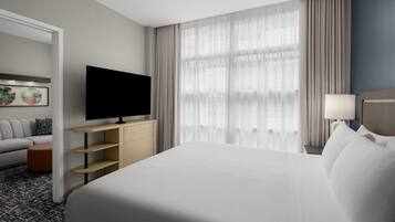 A hotel room with a bed, a TV, a sofa, a desk, and a window with curtains.