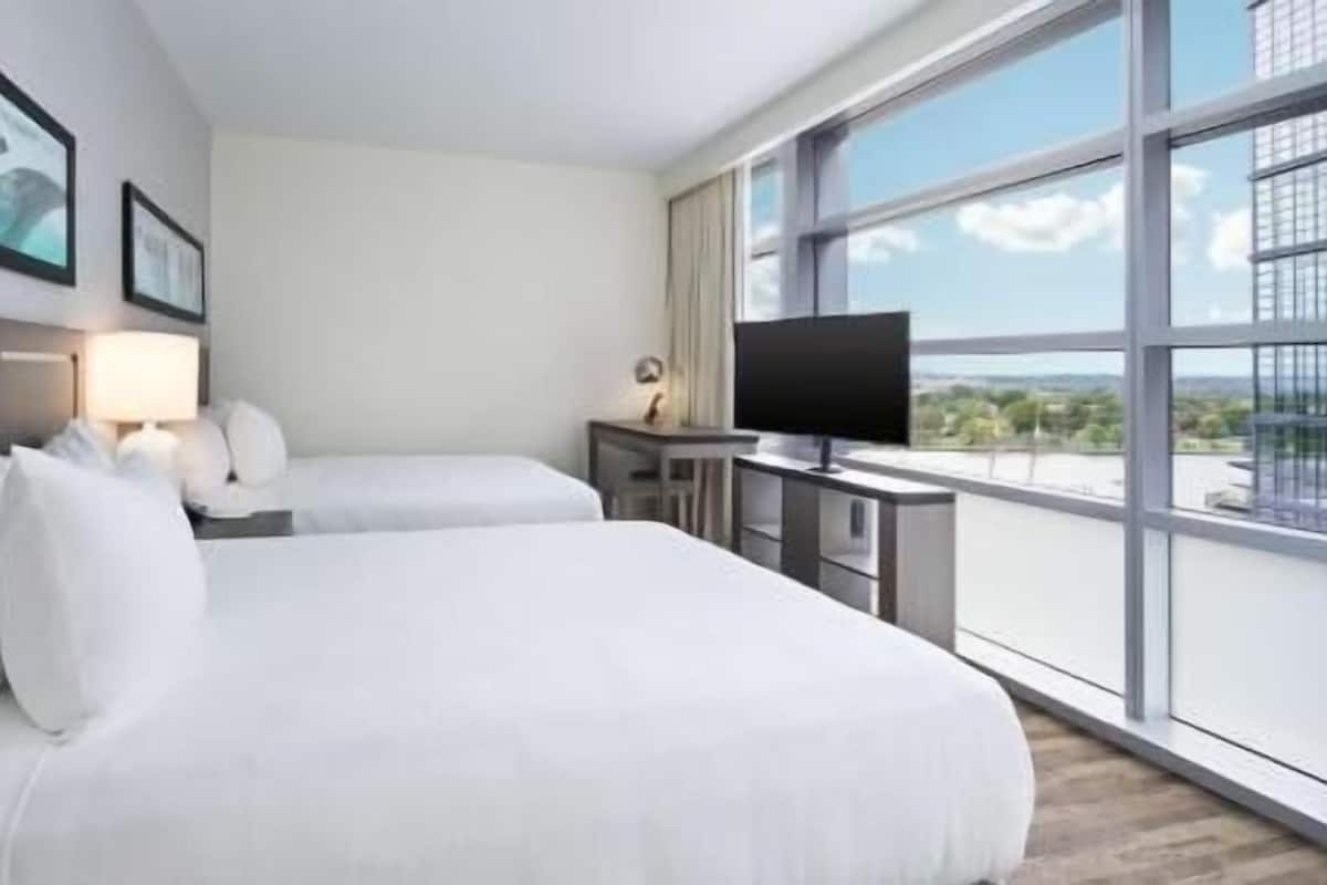 Habitación de hotel con dos camas, televisión y un ventanal con vistas a la ciudad.