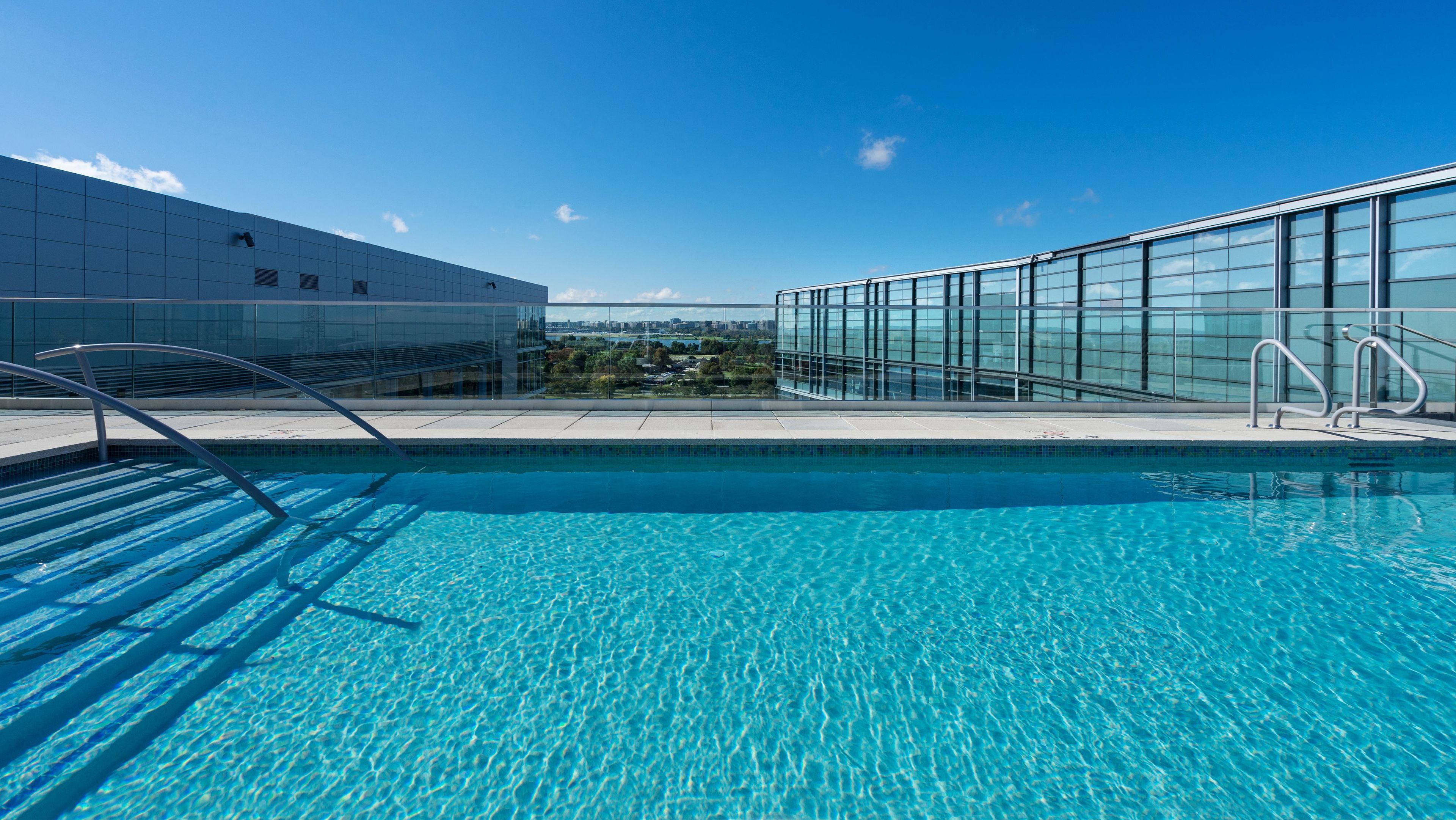 A clear blue pool with metal railings, surrounded by modern buildings with glass facades.