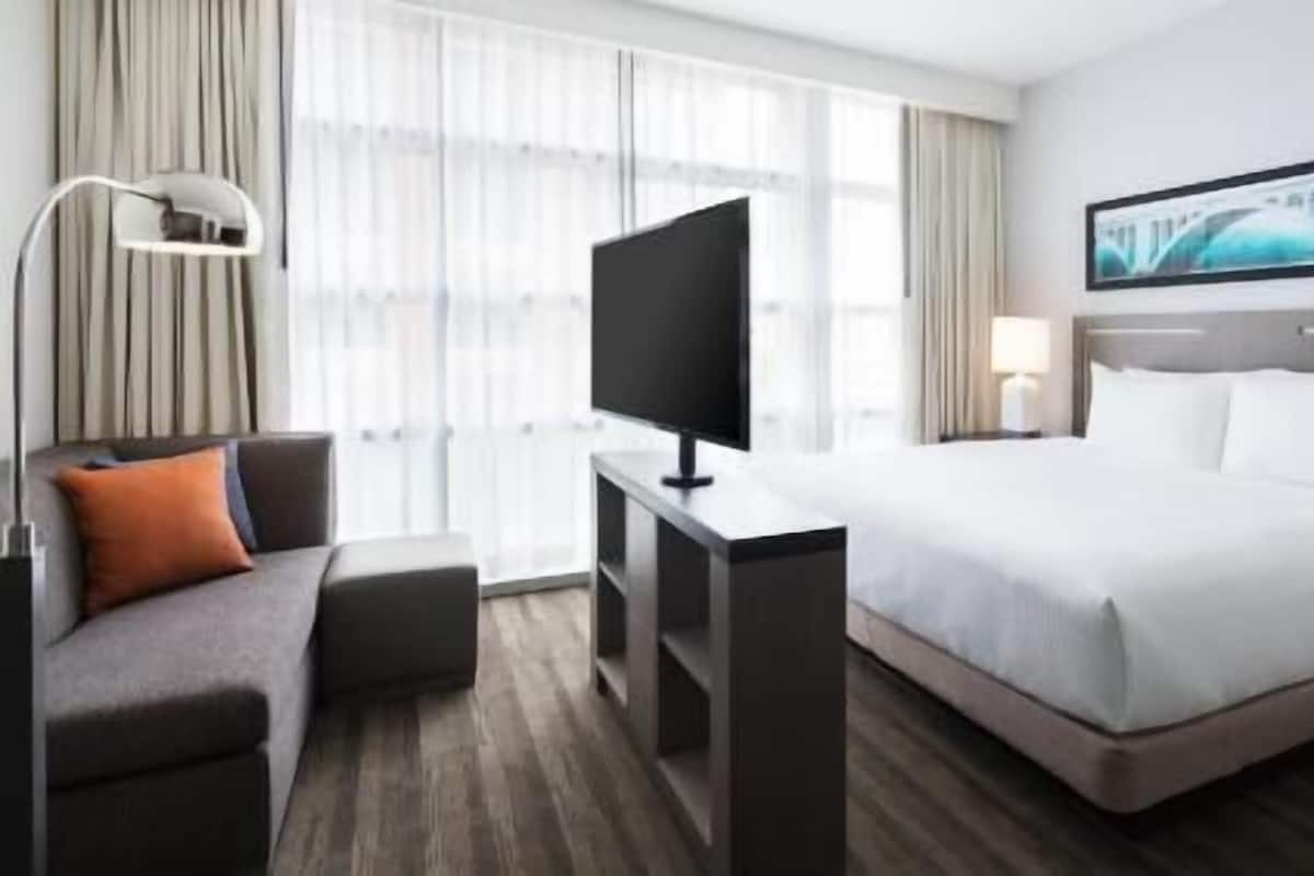 Habitación de hotel con cama, escritorio con televisor, sofá y un cuadro en la pared.