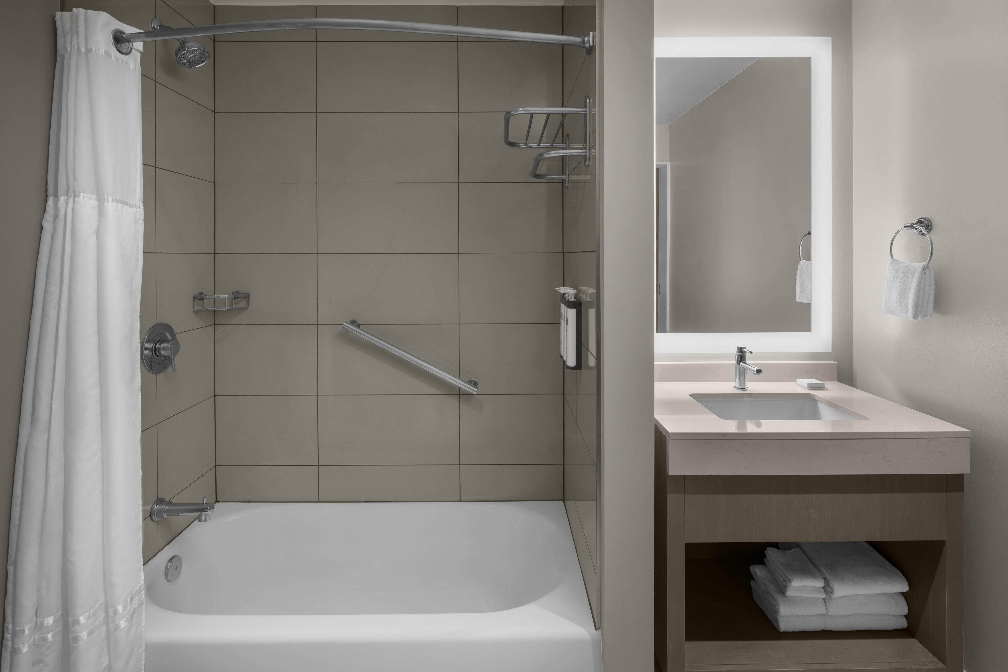A bathroom with a bathtub, a sink, a mirror, and a towel rack.
