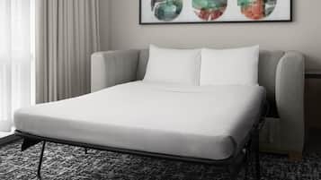 A hotel room with a single bed, a grey upholstered headboard, white bedding, and a framed abstract art piece on the wall.