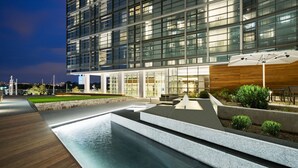 A modern hotel with a glass facade, outdoor seating area, and a water feature.